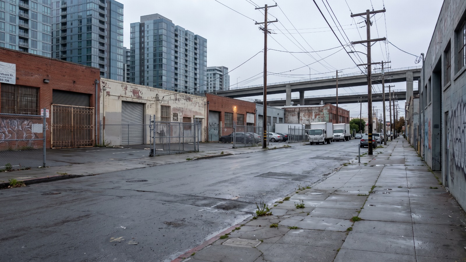 Low brick and concrete PDR buildings and surface parking lots along Harrison Street in Central SoMa, San Francisco, with newer towers rising behind them.