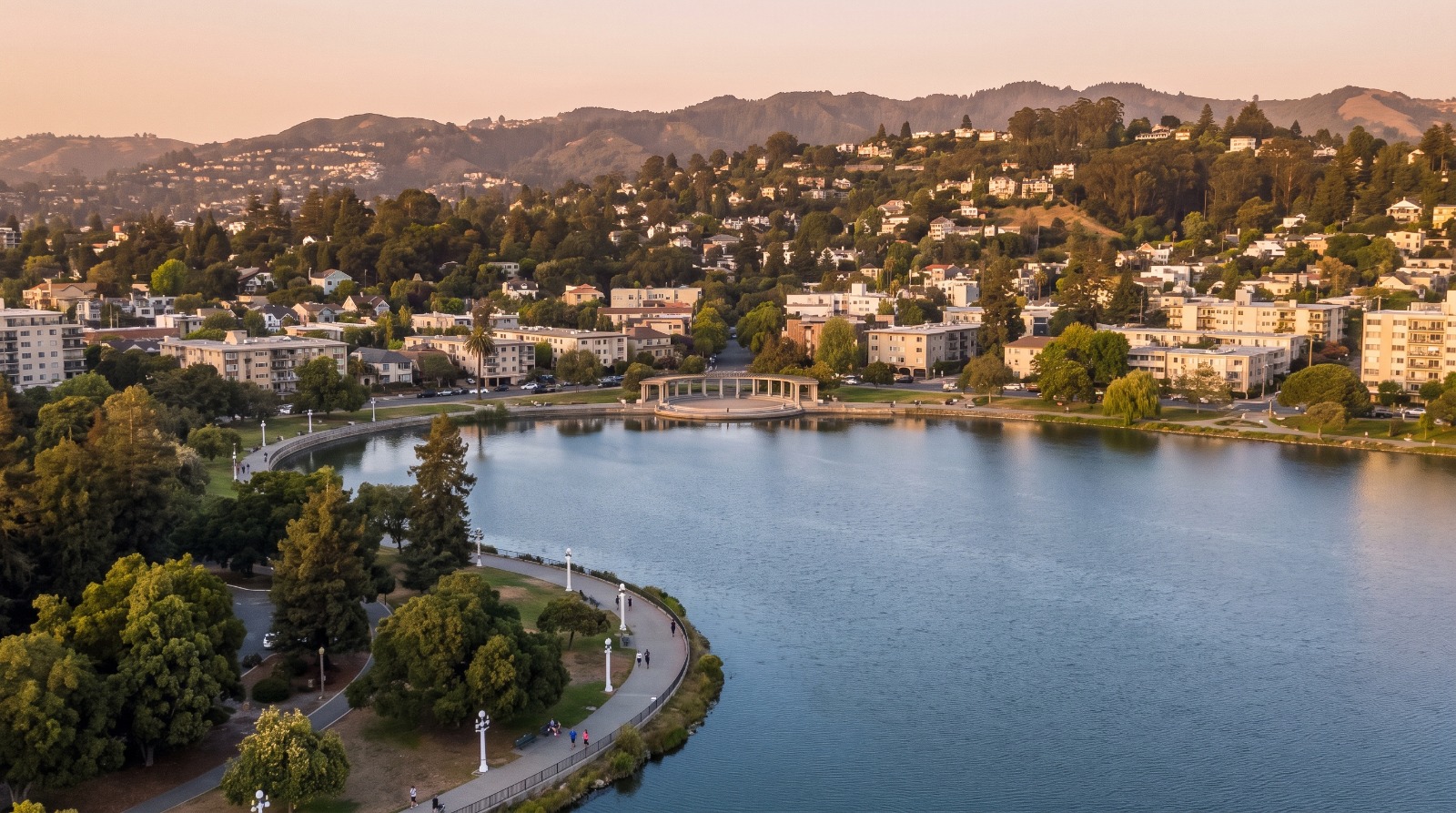 AI-rendered aerial view of Lake Merritt in Oakland at golden hour, with the pergola, Grand Lake apartments and the Oakland hills behind