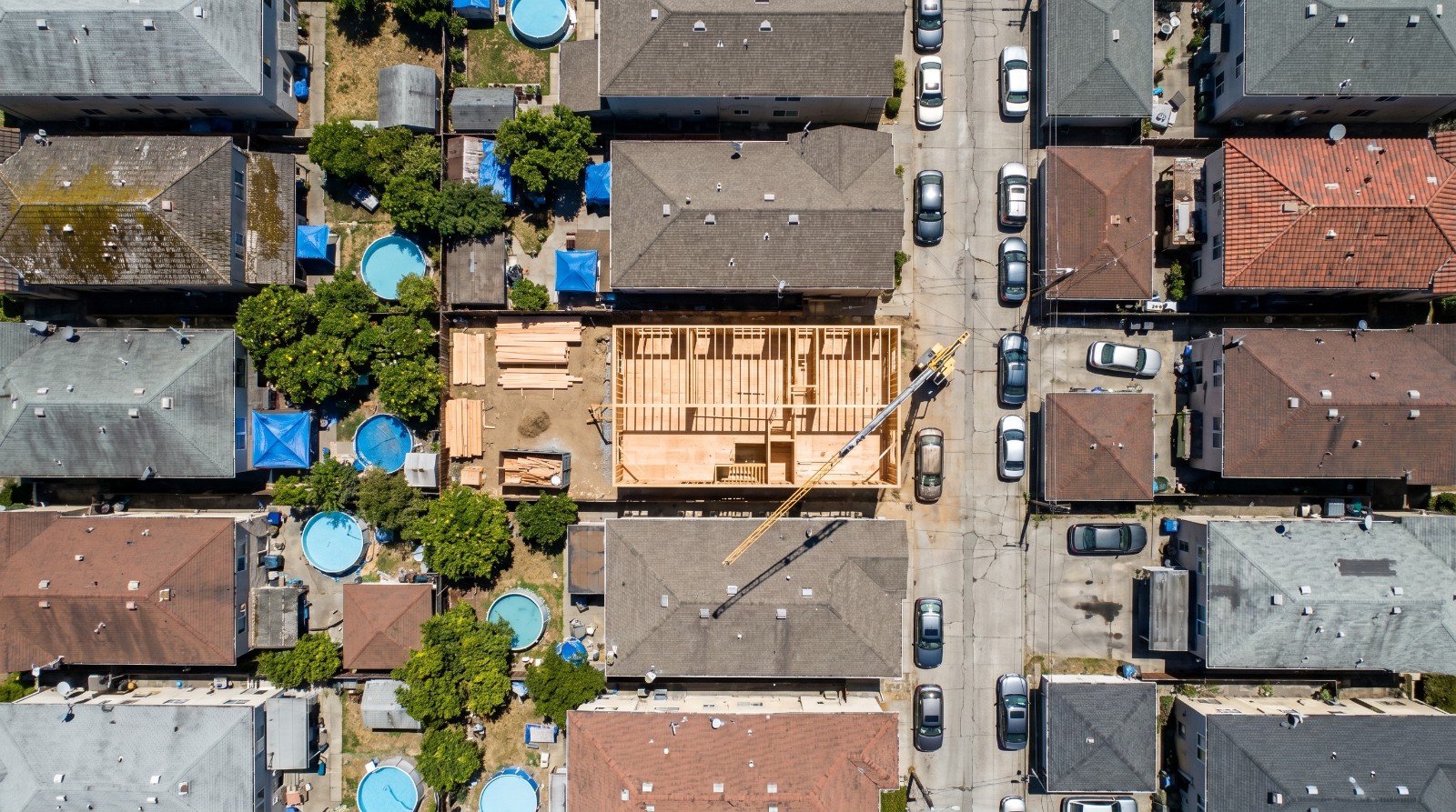 Overhead aerial view of an Oakland block where a new multifamily building is being framed on an infill lot, the kind of Bay Area housing the new housing bill is designed to make easier to build.
