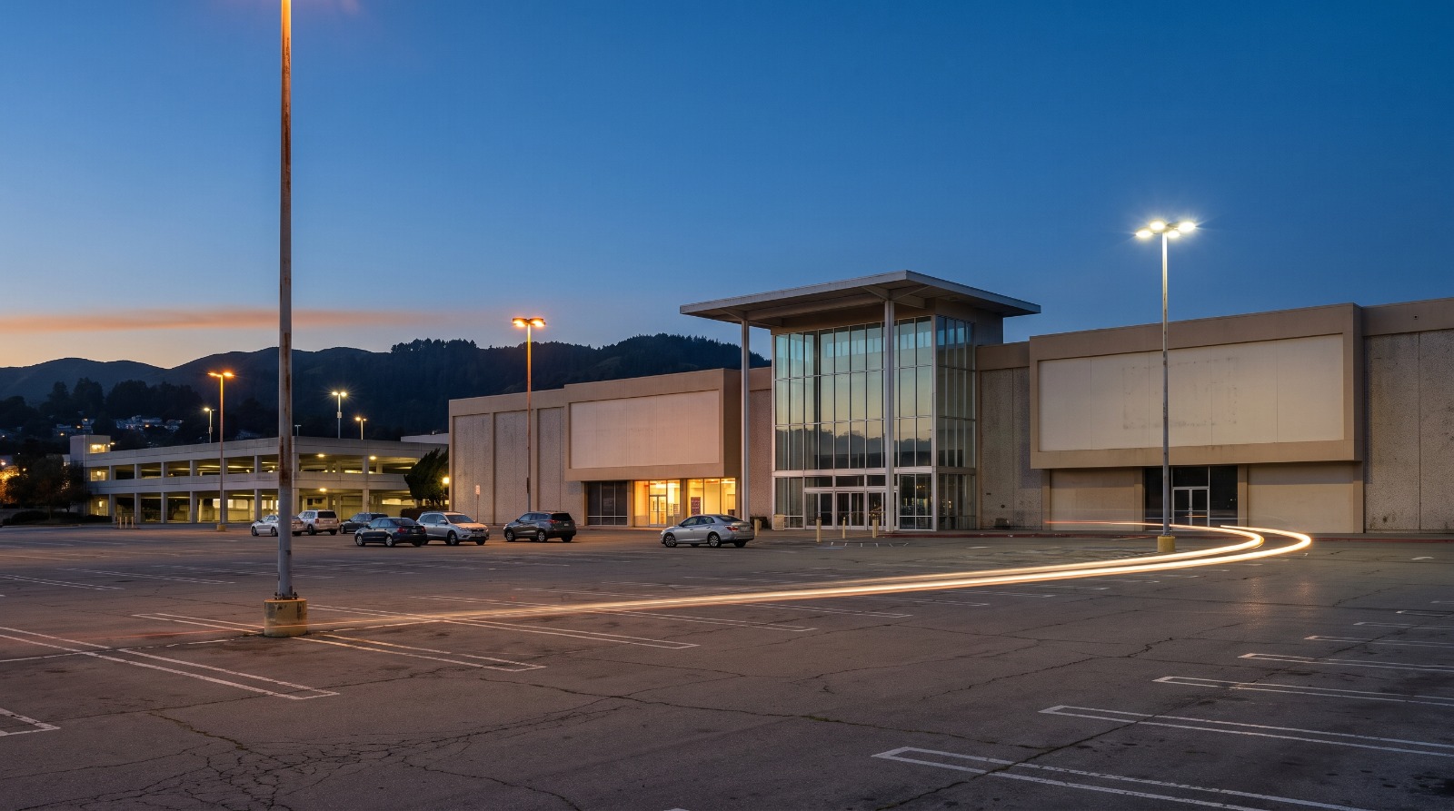 AI-rendered blue hour view of the Tanforan mall in San Bruno across its mostly empty parking lot with the hills behind