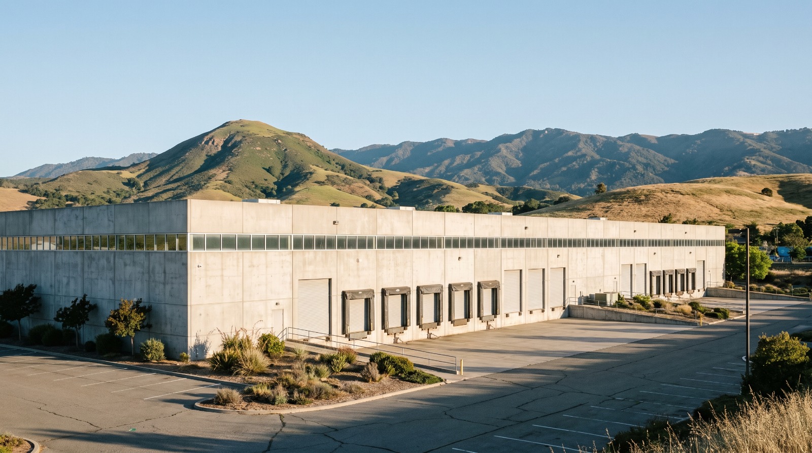 A large modern manufacturing building on a Morgan Hill business park street with El Toro peak rising behind it, near the site of Heron Power's new factory.
