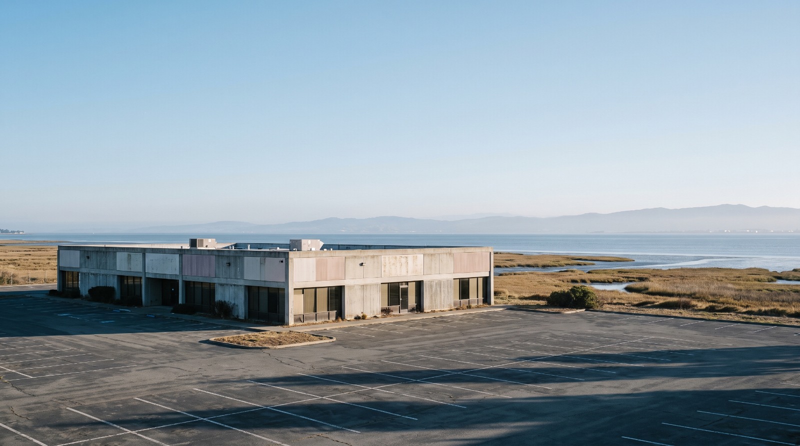 A low single-story Silicon Valley office building and its parking lot on the Menlo Park bayfront, the kind of site being torn down for apartments.