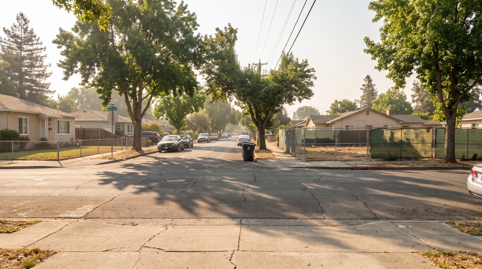 A residential street of single-story postwar homes in the Belle Haven neighborhood of Menlo Park, California, with a vacant infill lot mid-block.