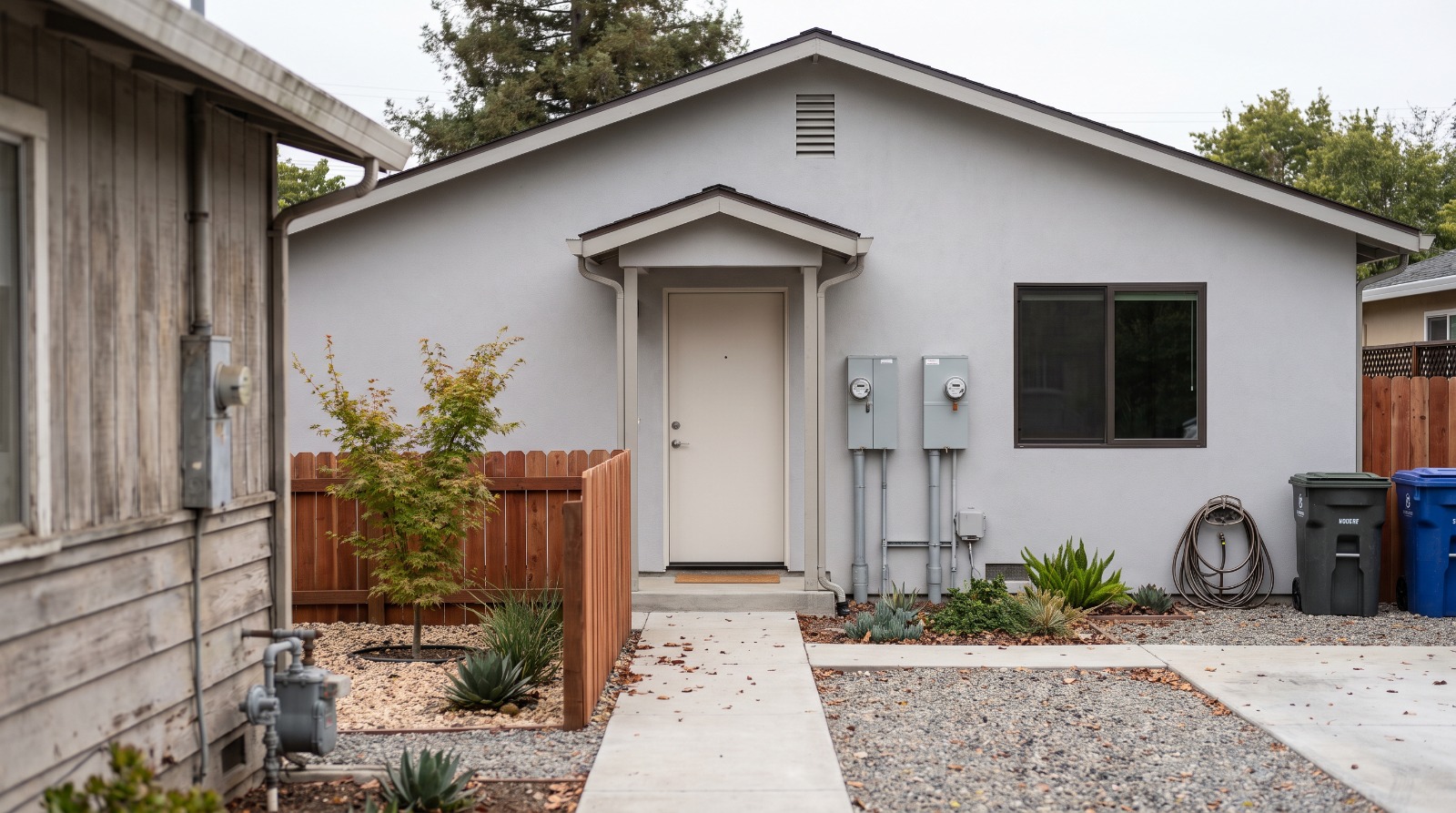 A new backyard ADU in San Jose with its own electric and gas meters beside the entry, behind an older ranch house