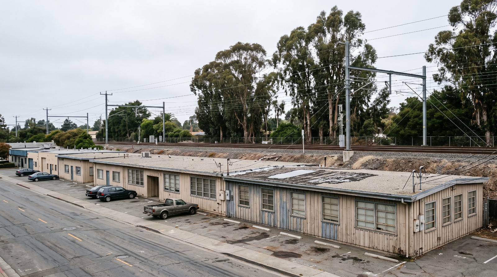 Single-story 1950s office buildings on Park Boulevard in Palo Alto beside the raised Caltrain corridor and eucalyptus trees