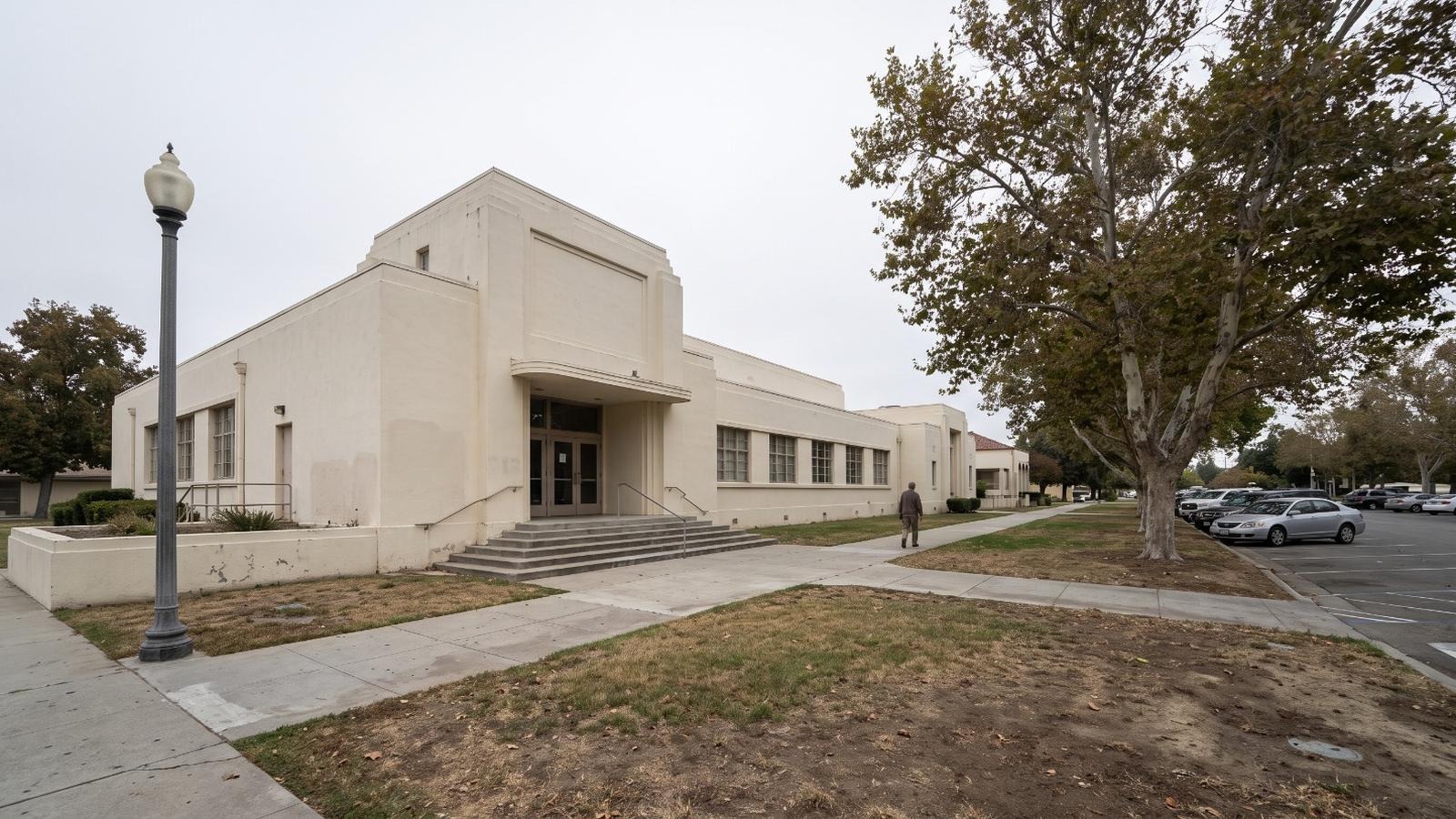 AI-rendered view of Wheeler Auditorium on West Sixth Street in Gilroy under an overcast sky, with the civic center parking lot to the right
