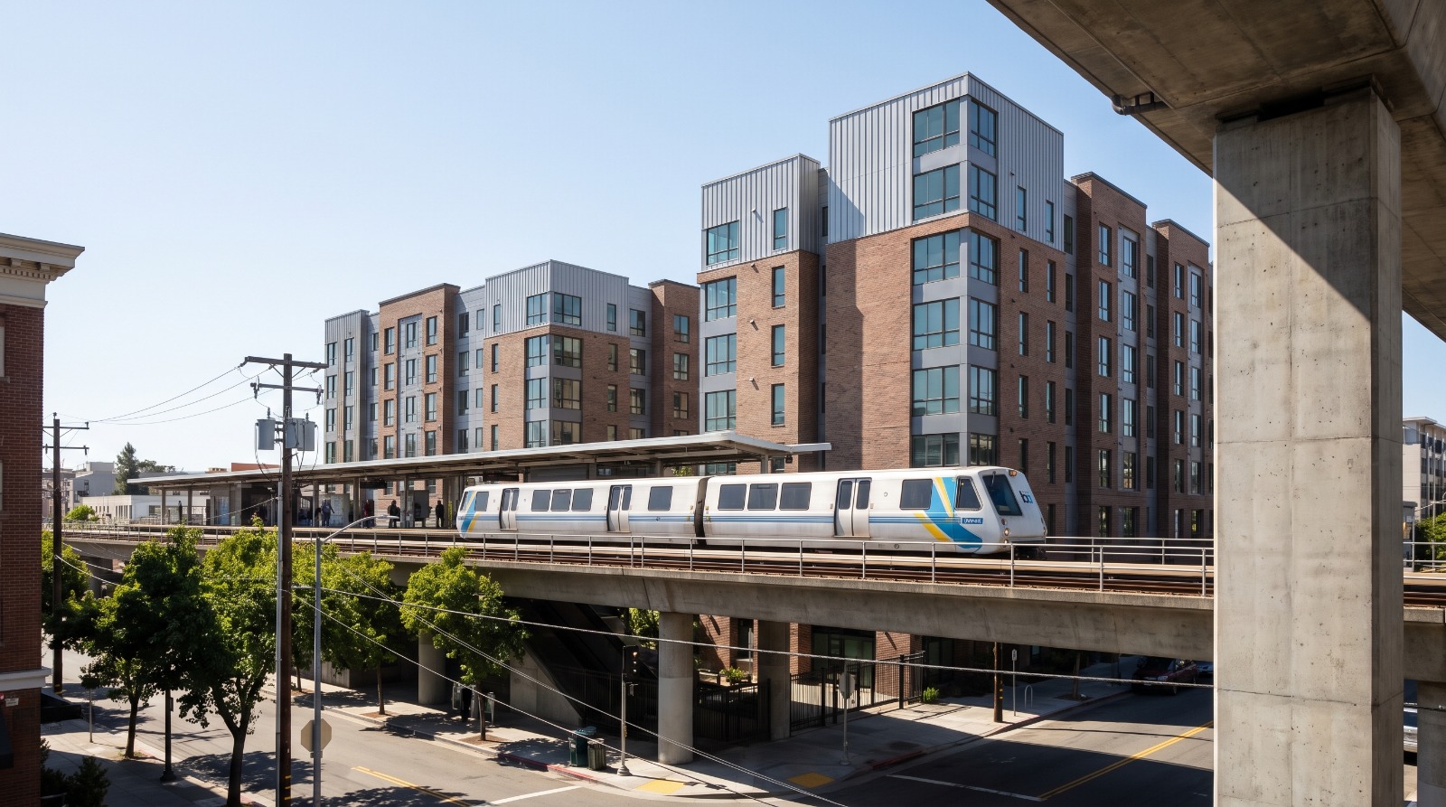 A BART train arriving at an East Bay station ringed by new mid-rise housing, the kind of transit-oriented growth Plan Bay Area 2050+ steers.