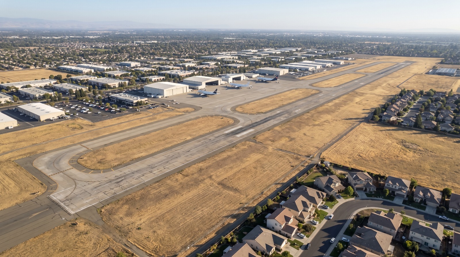 AI-rendered oblique aerial view of Mather Airport in Rancho Cordova at late afternoon, with its runways, cargo aprons and the Rancho Cordova street grid beyond