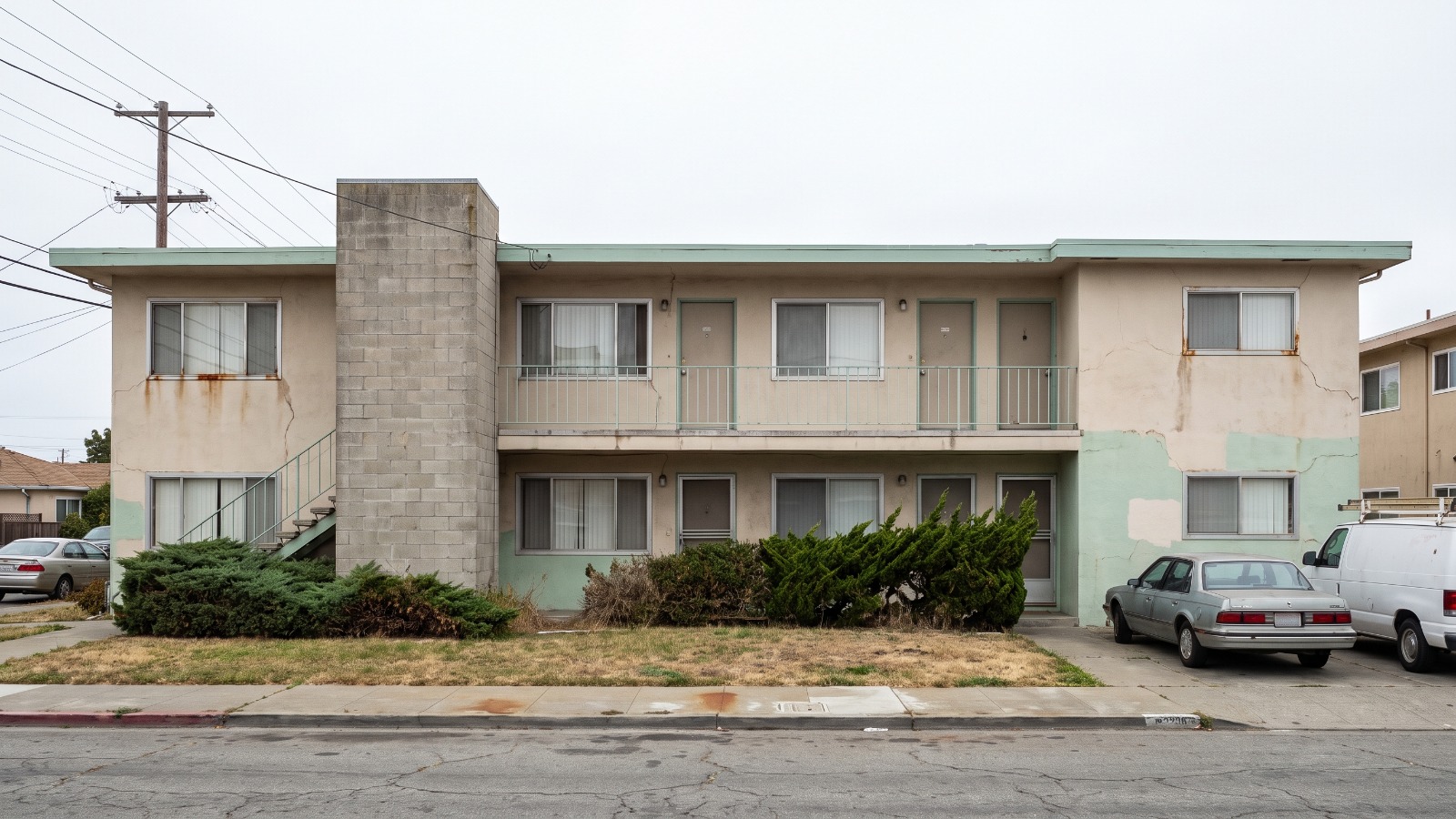 A mid-century two-story stucco walk-up apartment building on a Richmond, California residential street, the kind of older East Bay building covered by local rent caps.