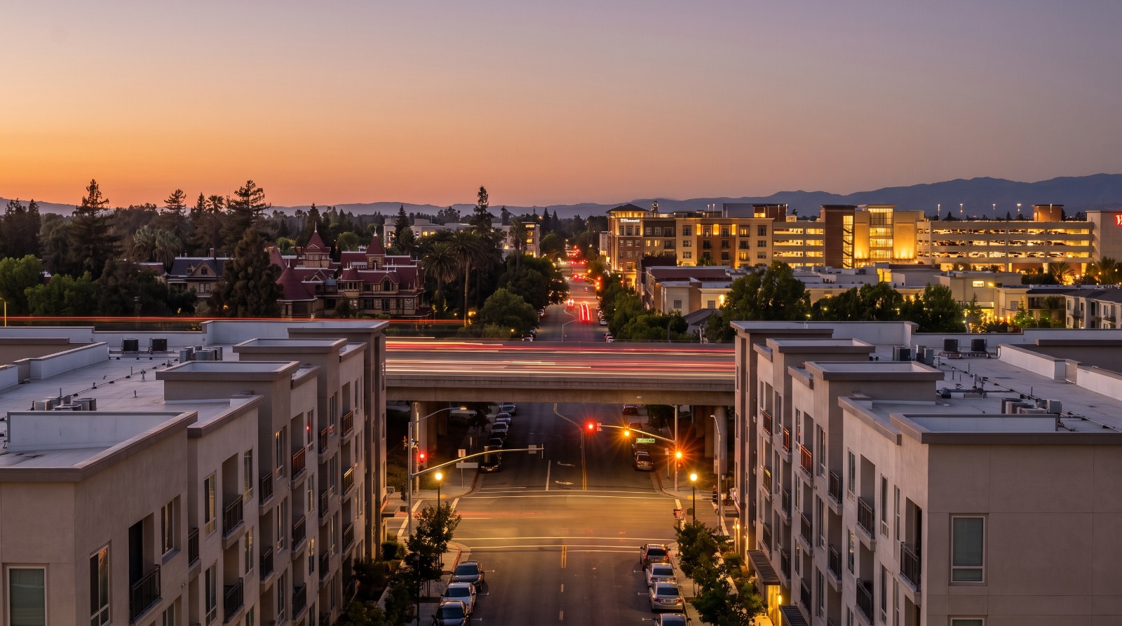 Blue hour view north along Winchester Boulevard in West San Jose toward Santana Row, with six-story apartment buildings in the foreground.