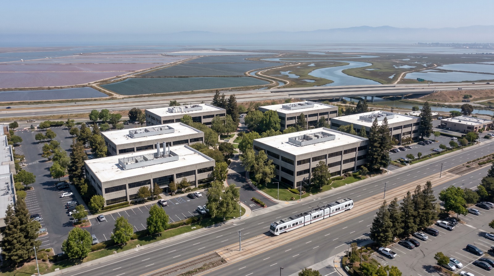 Aerial view of a low-rise North San Jose tech campus on North First Street with light rail and the Alviso baylands beyond.