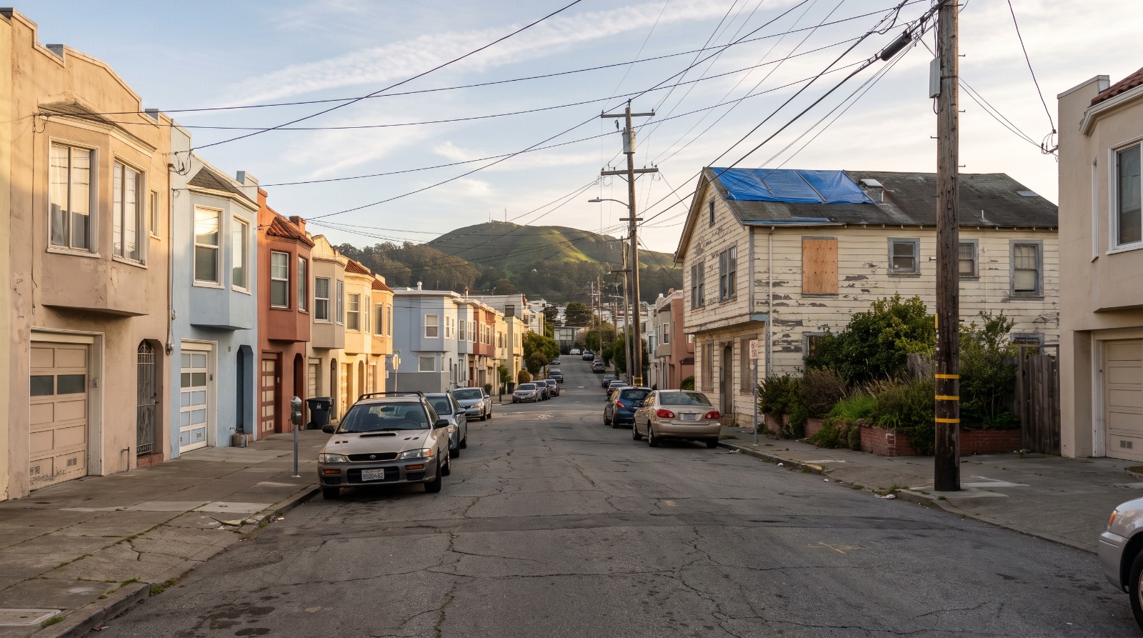 A row of stucco houses in San Francisco's Oceanview with one weathered fixer-upper, the kind of cheap house in San Francisco buyers compete for.