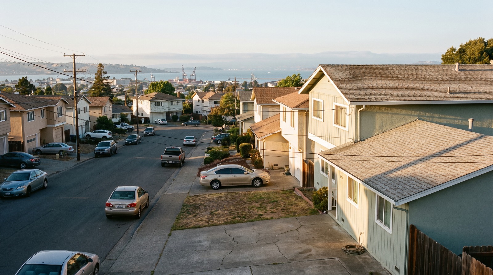 Hillside street of modest single-family homes in Vallejo at golden hour, looking west toward the Carquinez Strait, the affordable end of Bay Area millennial homeownership.